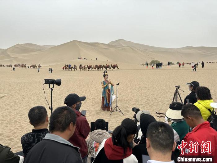 圖為2023年4月底，敦煌大漠“逐舞者”奧楠在鳴沙山月牙泉景區(qū)視頻直播，吸引游人圍觀。　馮志軍 攝